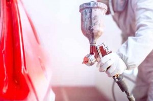 Close-up of spray gun with red paint painting a car